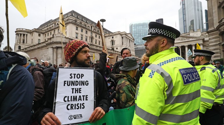A protester looks at a police officer during an Extinction Rebellion climate change protest outside the Bank of England in the City of London.