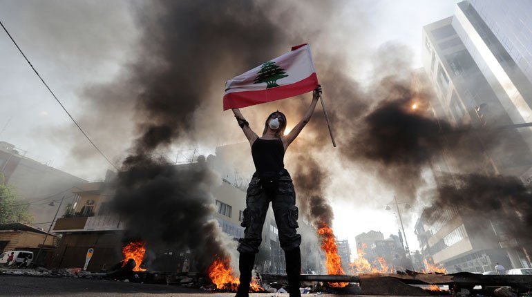 Anti-government protester in Lebanon standing in from of burning tires blocking roads.